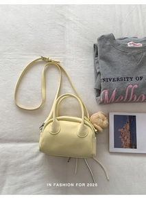Detail of light yellow bowling bag with a cute plush dog pendant and crossbody strap