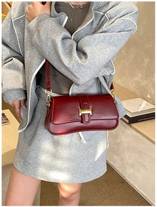 Detail of deep red leather shoulder bag with a gold metal H-shaped buckle closure