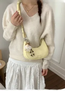 Detail der gelben Halbmond-Tasche mit Plüsch-Anhänger und verstellbarem Gurt an einem Model