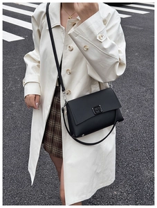 Street style shot of a black leather shoulder bag with a metal M buckle on a white coat