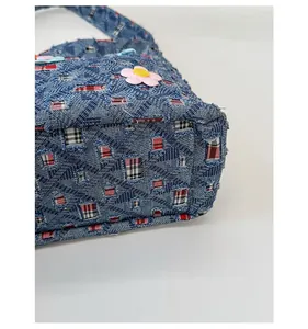 Dettaglio della borsa in denim con trama trapuntata, toppe floreali e fodera a quadri