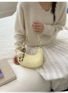 Detailansicht einer hellgelben Halbmond-Tasche mit Plüschanhänger und Perlen-Schlüsselanhänger