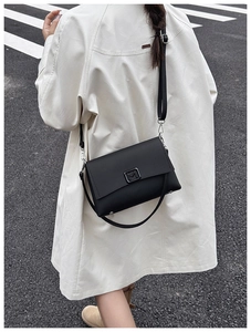 Street style view of a black leather crossbody bag with a metal M-logo buckle on a trench coat