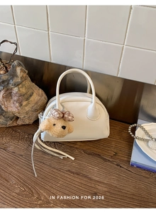 Detail view of a white leather bowling bag featuring a cute plush dog charm on a wooden table