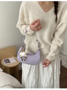 Detail der helllila Mondsichel-Tasche mit süßem Plüsch-Gnom-Anhänger an der Schulter