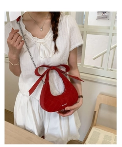 Detail of red quilted crescent bag featuring a large bow and silver chain strap