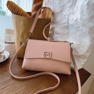 Close-up of pink envelope shoulder bag with metal M buckle on a rustic wooden desk