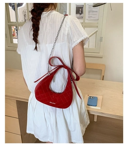 Detail of red quilted crescent bag with oversized bow and silver chain strap for women