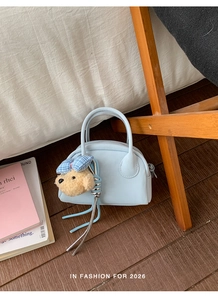 Detail of light blue bowling bag with a plush bear charm and woven tassel accent