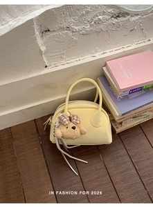 Detail of light yellow bowling handbag featuring a plush bear charm and leather tassels