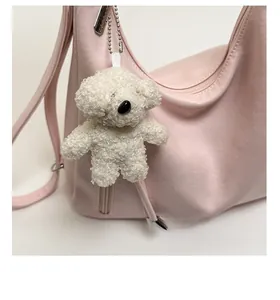 Close-up of a cute white fluffy bear plush pendant hanging on a pink leather bag strap