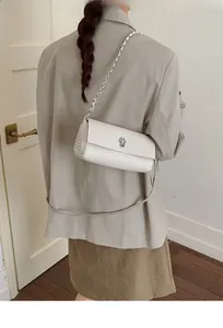 Detail view of cream white textured leather crossbody bag with silver chain strap and metal lock