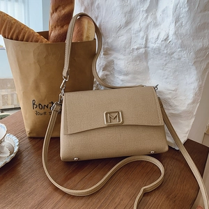 Detailed macro view of khaki canvas shoulder bag with gold M buckle on wooden table
