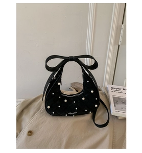 Detailed close-up of quilted crescent bag with pearls and ribbon bow on beige coat