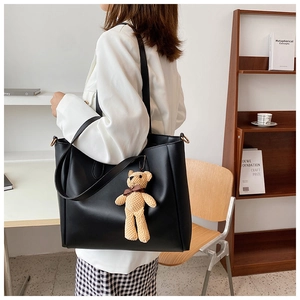 Detail of black PU leather tote bag with a brown teddy bear charm and double shoulder straps