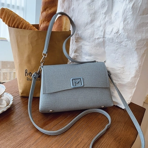 Detailed macro view of gray-blue textured fabric handbag with silver metallic M-logo