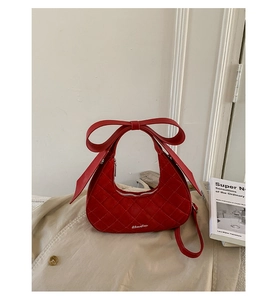Close-up of red quilted crescent bag with large bow handle and silver zipper detail