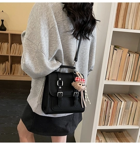 Detail view of black textured leather square bag with cute plush bear keychain charm