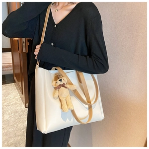 Detail view of off-white tote bag featuring a cute khaki knitted bear charm and brown straps