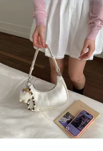 Detail einer perlweißen Hobo-Tasche mit Plüschpuppen-Anhänger und Perlen-Accessoires