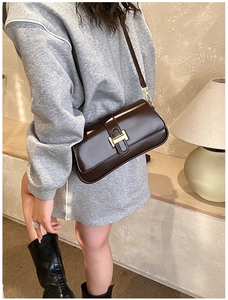 Close-up of a dark brown glossy leather underarm bag with a gold H-shaped metal buckle