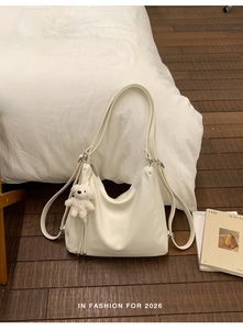 Close-up of creamy white faux leather hobo bag with a cute plush bear charm on wood floor