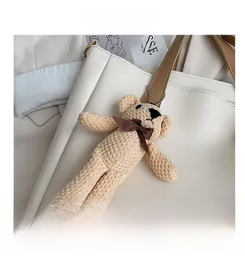 Close-up of beige knitted teddy bear charm with a brown bow attached to a tote bag