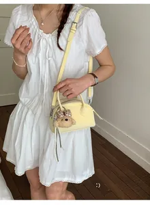 Detail of light yellow leather bowling bag with cute teddy bear charm on model