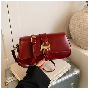 Detail view of smooth dark red leather handbag with elegant gold buckle and shoulder strap