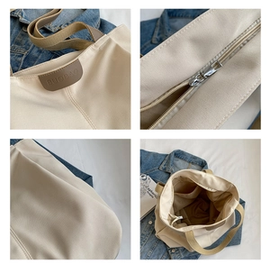 Detail view of beige canvas tote bag with leather logo, metal zipper and spacious interior