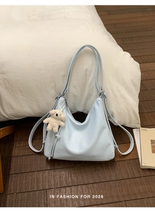 Detail of light blue soft leather tote bag featuring a white plush bear charm and long straps