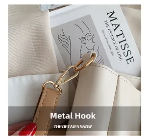 Macro shot of gold hardware hook and leather strap detail on a cream tote bag