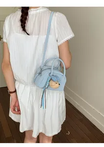 Detailed view of a light blue leather bowling bag with a cute plush bear charm accessory