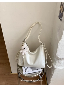 Close-up of creamy white faux leather hobo bag with cute plush bear charm on a metal chair