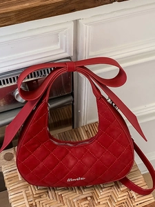 Elegant red crescent hobo bag with large bow and quilted diamond pattern on a table