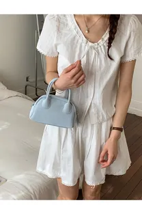 Detail view of light blue mini bowling bag held by model in a minimalist bedroom setting
