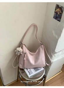 Detail view of pink PU leather hobo bag with fringe zipper and white dog plush charm