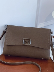 Brown cross-grain leather shoulder bag with metallic M buckle on dark wood surface