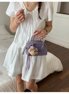 Detail of purple mini bowling bag with bear charm and tassel shown on model in white dress