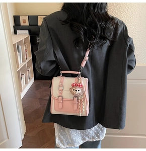 Detail of elegant two-tone crossbody bag with plush doll charm and adjustable shoulder strap
