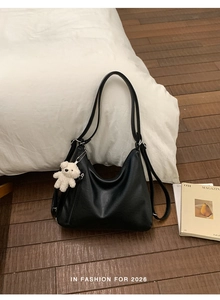 Detail of black leather hobo backpack with white plush bear charm on wooden floor