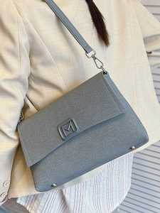 Minimalist grey envelope shoulder bag with M logo and silver studs on beige suit