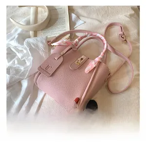 Dettaglio borsa a secchiello rosa con chiusura dorata e sciarpa di seta sul manico