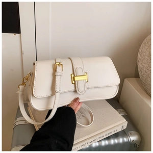 Close-up of cream underarm bag with gold buckle on a silver suitcase and books
