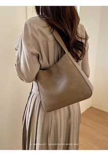 Détail du sac seau marron avec texture plissée et plaque logo métallique rectangulaire