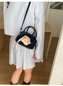 Detail of black bowling bag with cute beige plush bear charm and adjustable shoulder strap