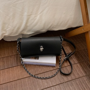 Detail of black lychee grain leather crossbody bag with silver metal swivel lock on books