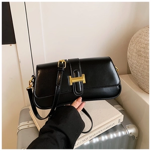 Detail view of the black glossy leather handbag featuring a prominent gold H-shaped clasp