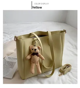 Detail view of yellow tote bag with bear charm and adjustable shoulder strap on white fabric