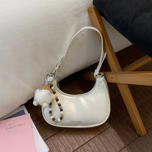 Detail einer weißen Hobo-Tasche aus Leder mit Plüschmonster und Perlenkette-Zubehör